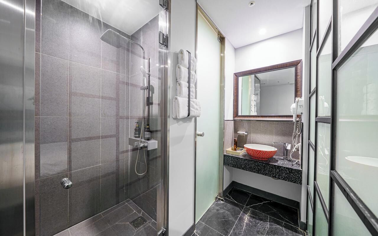 A modern bathroom with a glass shower enclosure, a vanity with a red bowl sink, and a large mirror.