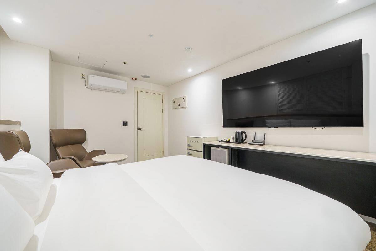 Habitación de hotel con cama, sillón, escritorio, televisor de pantalla plana y minibar.