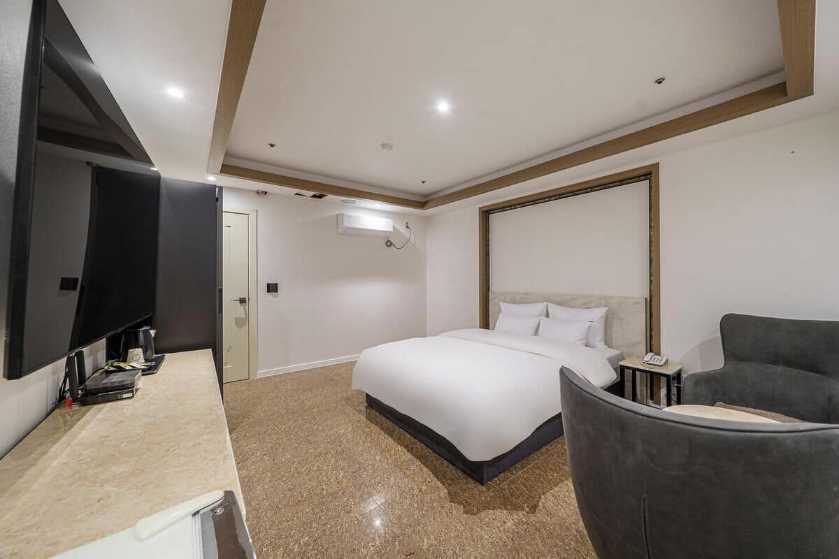 Habitación de hotel con cama, escritorio con computadora, silla, televisor y espejo grande.