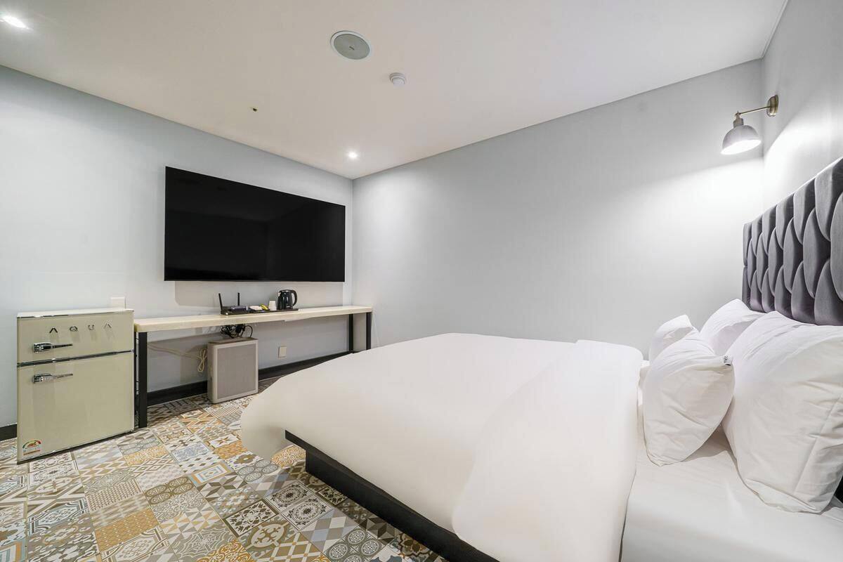 Una habitación de hotel moderna con una cama grande, un televisor de pantalla plana, un escritorio con computadora y un minibar.