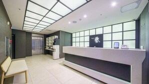 Tauleller de recepció amb un panell de vidre, una banca i una estanteria amb objectes.