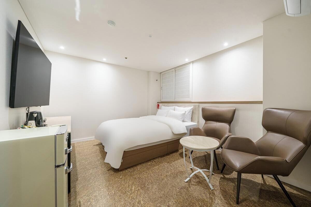 Une chambre d’hôtel équipée d’un lit, d’une chaise, d’une petite table, d’une télévision et d’un mini-bar.
