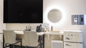 Habitació d'hotel moderna amb televisió de pantalla plana, cafetera, assecador de cabells, mini-nevera i un mirall rodó.