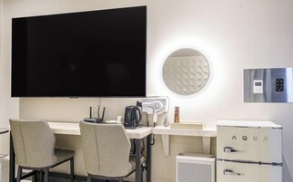 A modern hotel room with a flat-screen TV, a coffee maker, a hairdryer, a mini-fridge, and a round mirror.