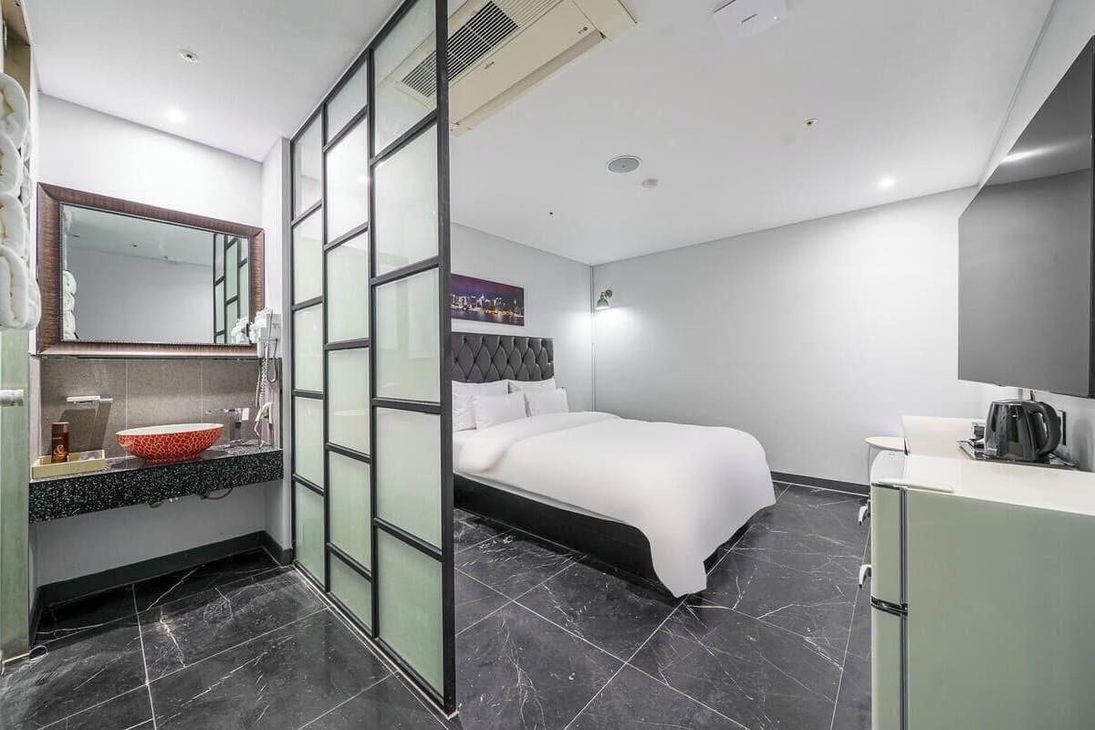 Una habitación de hotel moderna con una cama, un tocador con espejo, un lavabo y un televisor de pantalla plana.