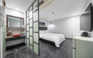 Quarto de hotel moderno com uma cama, toucador com espelho, pia e televisão de tela plana.