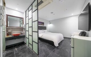 A modern hotel room with a bed, a vanity with a mirror, a sink, and a flat-screen TV.