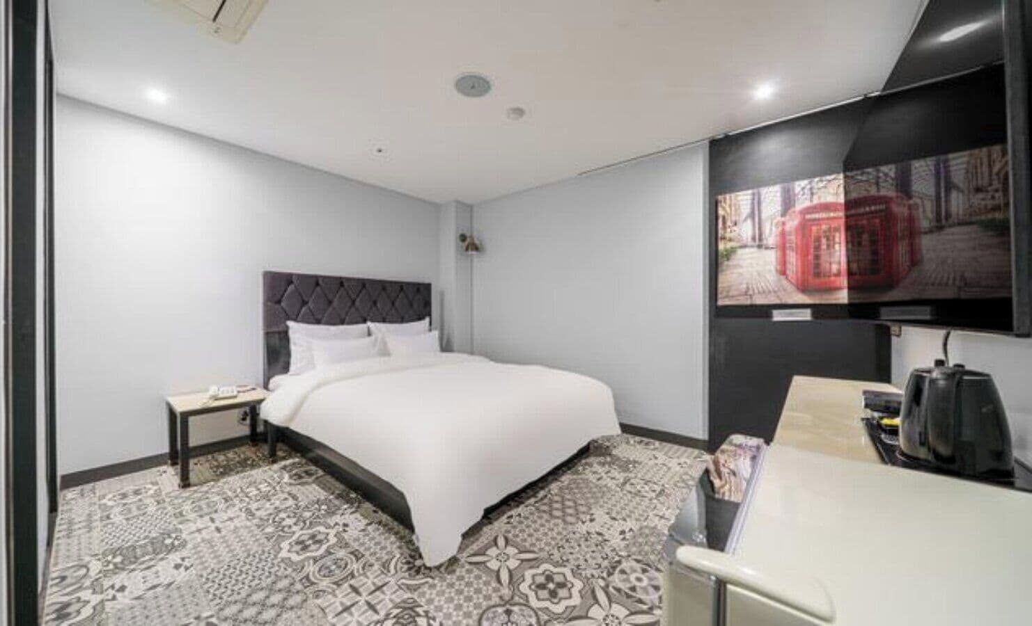 Una habitación de hotel con una cama, un escritorio, una silla, un televisor y una alfombra estampada.