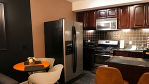 Una cocina moderna con armarios oscuros, un refrigerador de acero inoxidable, un microondas y una estufa a gas. Hay una pequeña zona de comedor con una mesa y dos sillas.