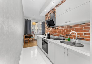 A modern kitchen with a brick wall, white cabinetry, a built-in oven, and a stainless steel sink. - Ujejskiego City Center Apartment (Kraków)