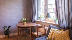 Une pièce avec une table en bois, des chaises, un canapé, une fenêtre avec des rideaux et une plante en pot.