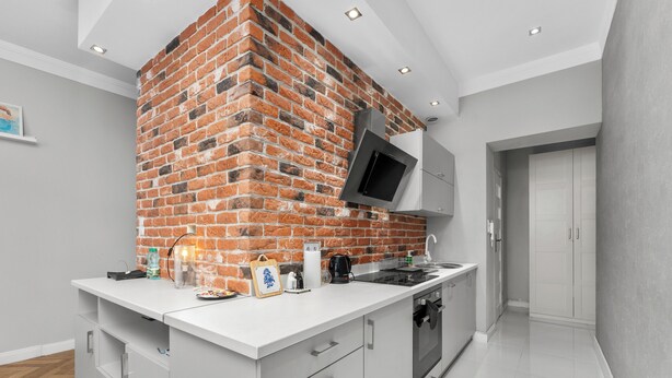 Une cuisine moderne avec un mur d’accent en briques, des meubles blancs et des appareils électroménagers intégrés.