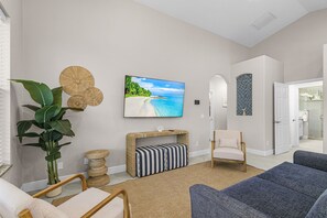 A living room with a large TV, a plant, a bench, and a chair. - 140 Pearl Paradise 3BR/2BA w/ Pool! (Fort Myers Beach)