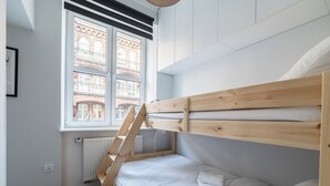 A bunk bed with a wooden ladder, white bedding, and a window with a view of a building. - Park Wilsona Charming Studio (Poznań)