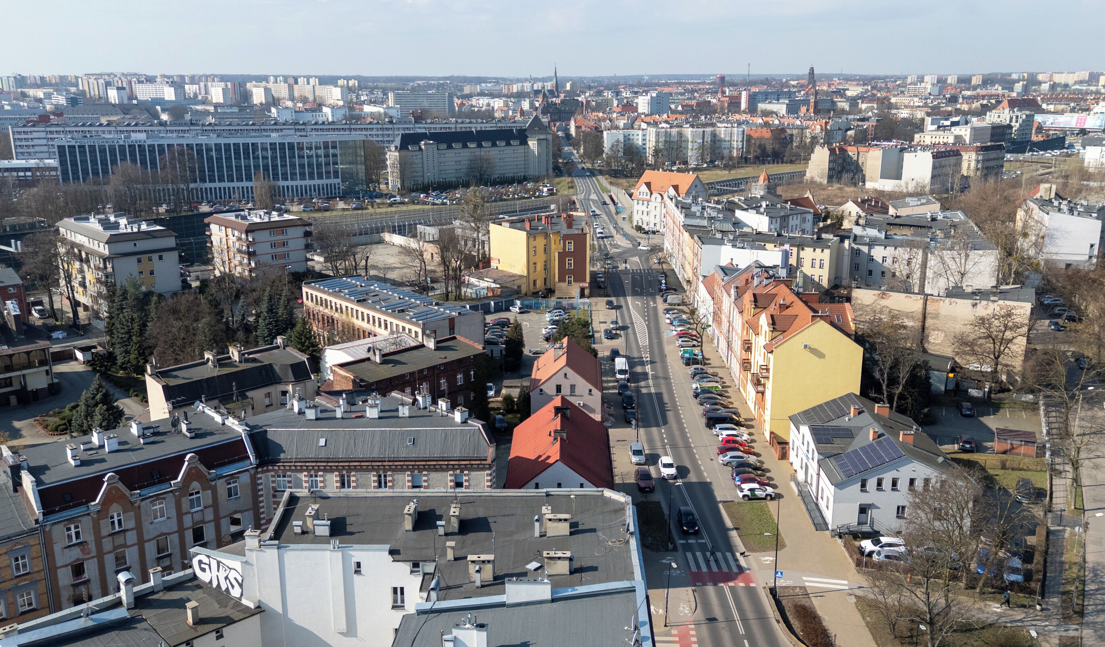 An aerial view of a cityscape with a mix of modern and historic buildings, a prominent red-roofed building, and a large industrial complex.