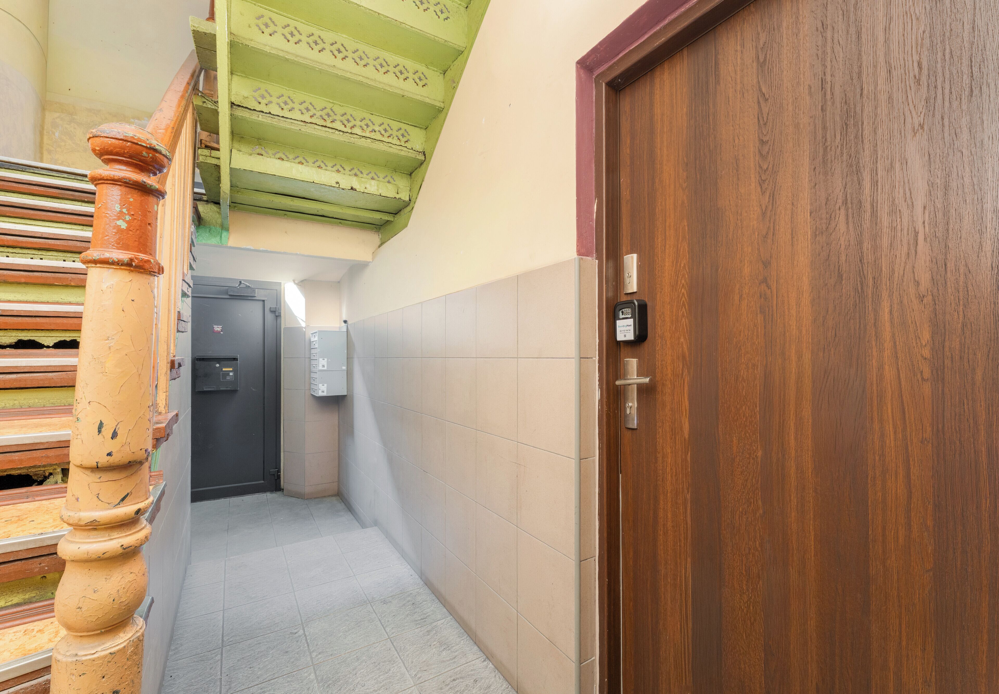A hallway with a wooden door, a staircase, and a wall-mounted intercom.