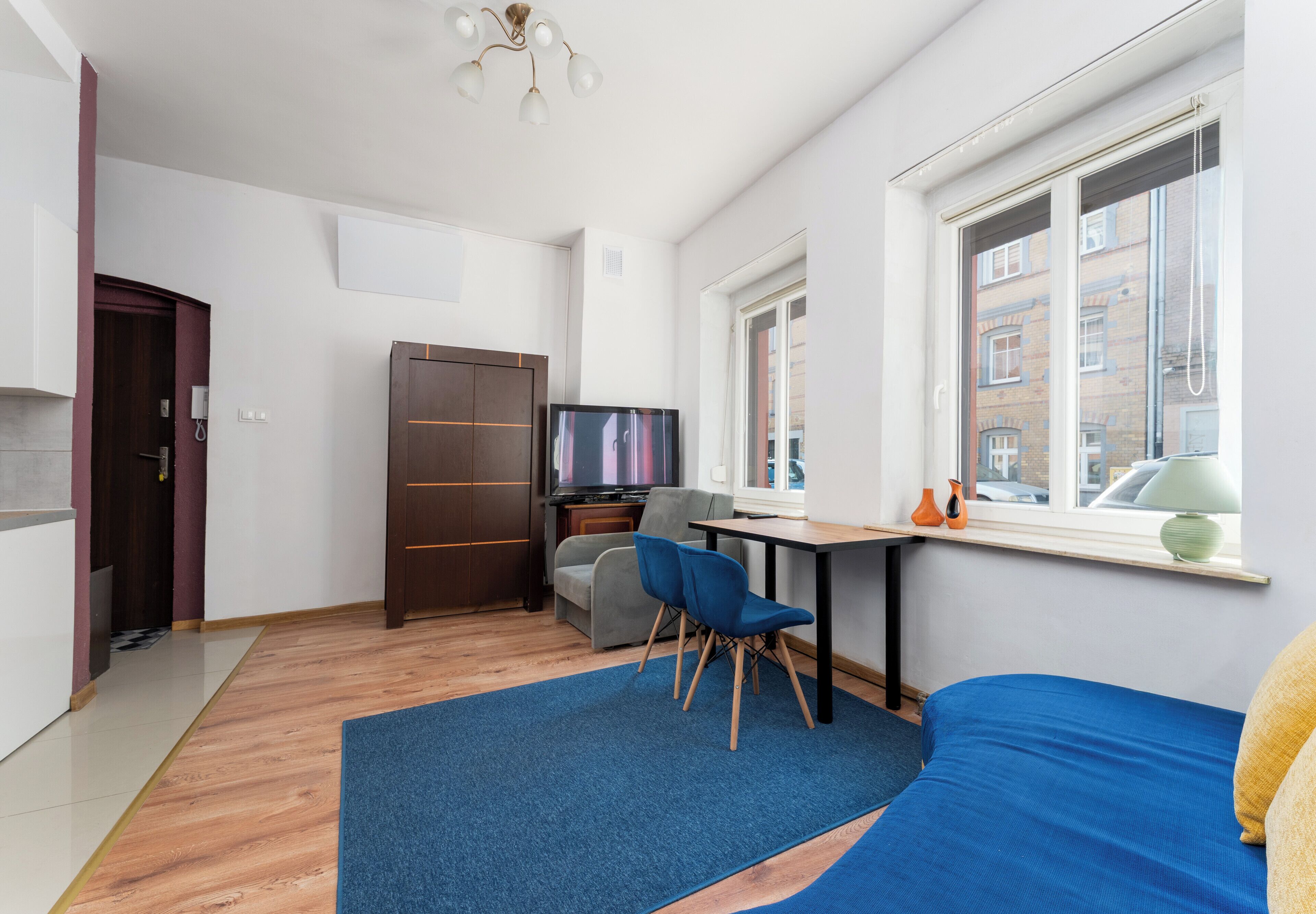 Une chambre moderne équipée d’un lit, d’un bureau, d’une télévision et d’une fenêtre donnant sur des immeubles.