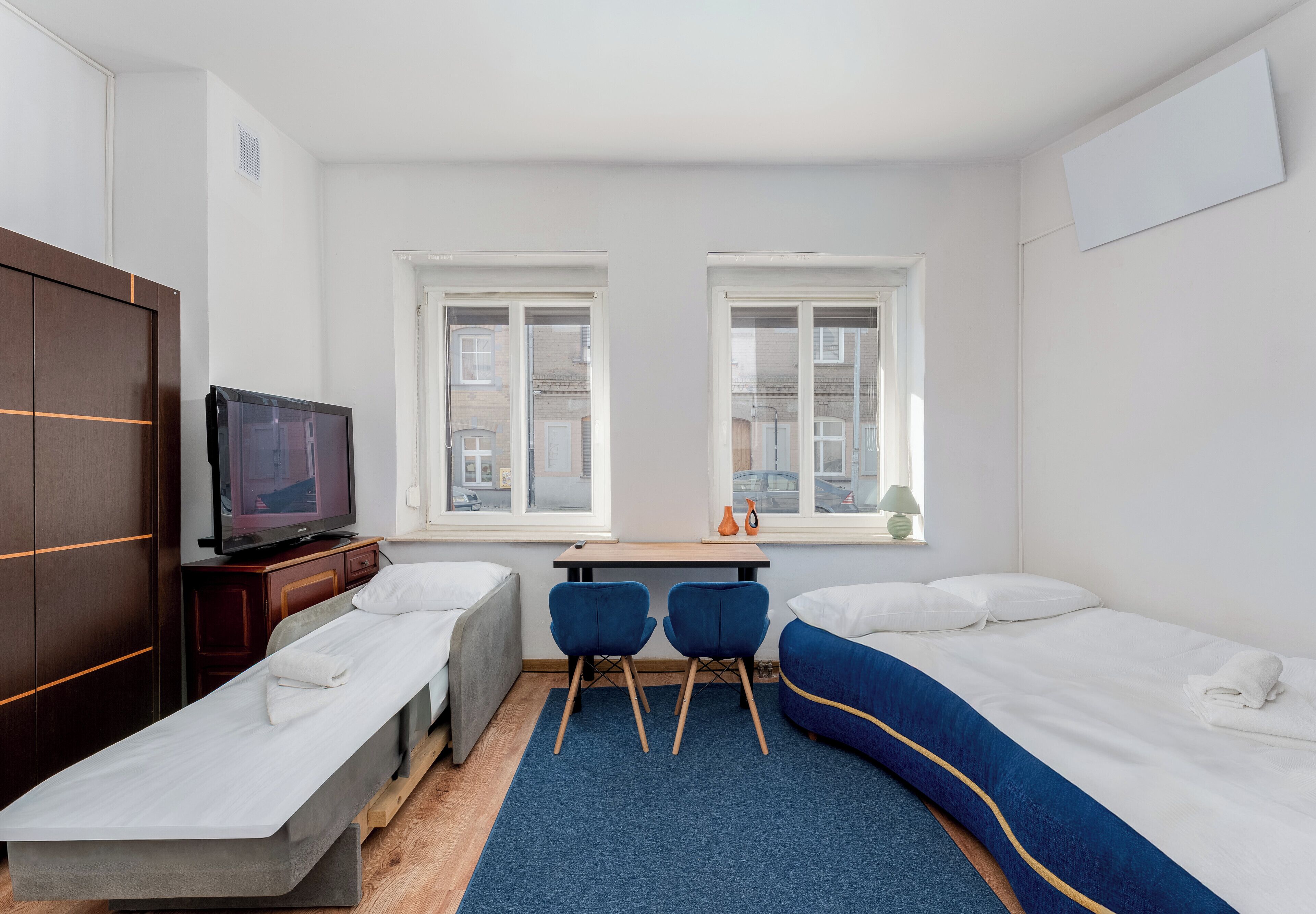 A hotel room with a bed, a desk, two chairs, a television, and a window.
