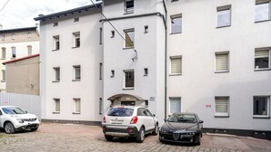 Een gebouw met meerdere ramen, een overdekte ingang en drie geparkeerde auto's.