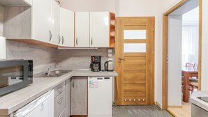 Een kleine keuken met witte kastjes, een magnetron, een koffiezetapparaat en een vaatwasser.
