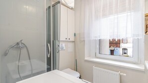 Een badkamer met douche, toilet en raam met uitzicht op gebouwen.