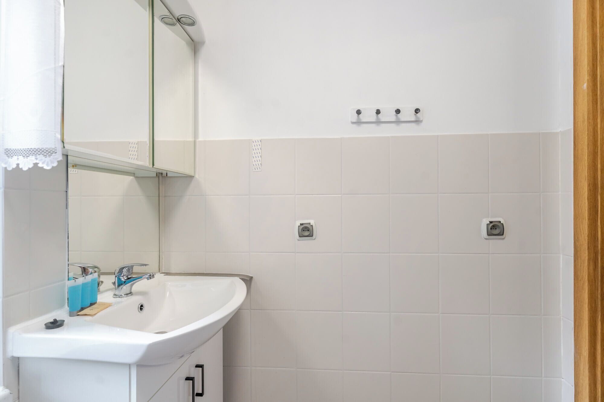 A bathroom with a white sink, mirror, and two electrical outlets on the wall.