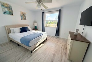 A bedroom with a bed, a ceiling fan, a window with curtains, a TV, and a small cabinet.