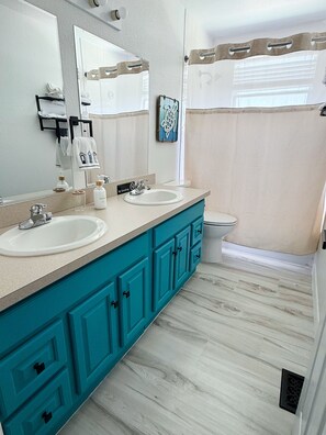 A bathroom with two sinks, a toilet, a shower curtain, and a mirror.