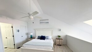 Un dormitorio con cama, ventilador de techo, mesita de noche, lámpara y una puerta.