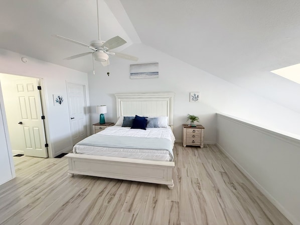 A bedroom with a bed, a ceiling fan, a nightstand, a lamp, and a door.