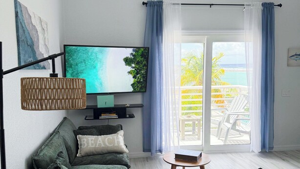 Una sala de estar con un sofá, un televisor, un ventilador de techo y vistas al exterior.