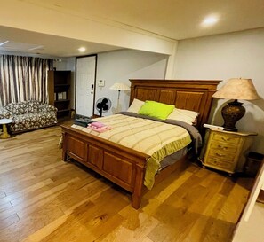 A bedroom with a wooden bed, a bedside table with a lamp, a chair, and a fan.