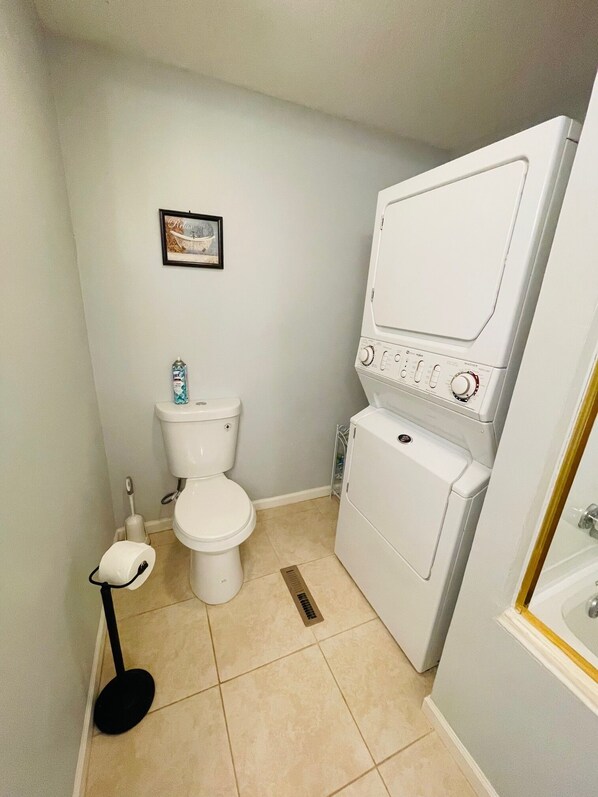 A small bathroom with a toilet, a washing machine, and a toilet brush.