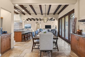 A large dining table sits between the breakfast bar, living room and a wall of glass patio doors beneath exposed beams. - Desert Retreat - Pool, Hot Tub & Putting Green (Cave Creek)