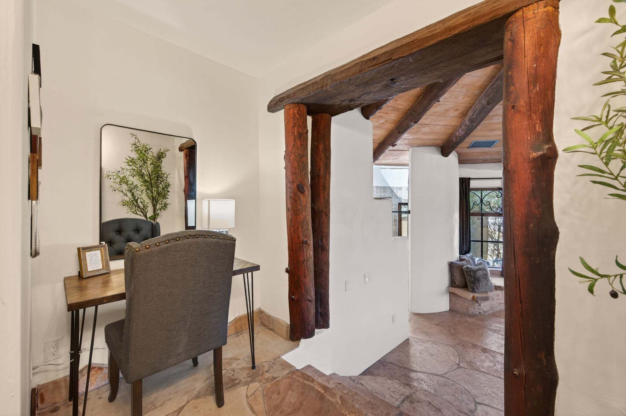 A compact writing desk sits beside a rustic log-framed opening that leads toward the living room.