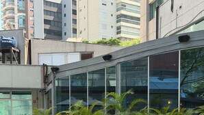 Una piscina con borde de azulejos, rodeada de plantas en macetas y edificios modernos al fondo.