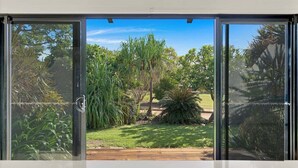A sliding glass door leading to a garden with various plants and a wooden deck. - Balu luxe (Broome)