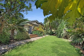 A modern house with a well-maintained lawn, a pathway leading to the entrance, and lush tropical vegetation surrounding the property.
