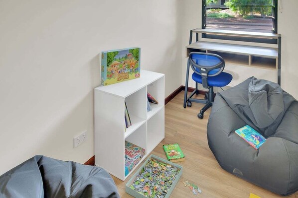 A room with a white bookshelf, a blue chair, a bean bag, and a puzzle box.