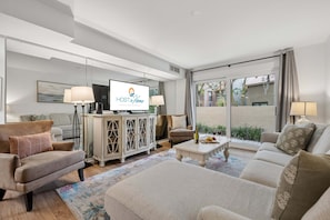 A modern living room with a television, sofas, a coffee table, and a view of the outside. - Harbour Town Villa, South Beach Pool Pass, Walk to Marina & Golf Links, Warm Coastal Furnishings (Hilton Head Island)