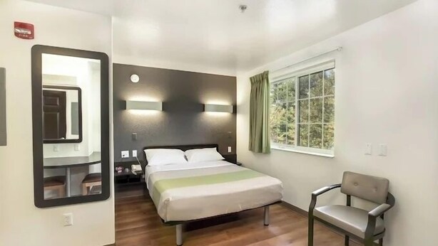 Une chambre d’hôtel avec un lit, une chaise, une fenêtre avec des rideaux et un miroir.