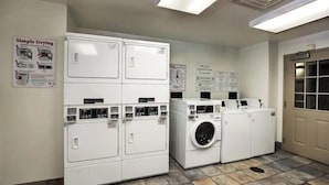 Une buanderie équipée de machines à laver et de sèche-linge superposés, dotée d’un sol carrelé et ornée d’affiches informatives sur les murs.