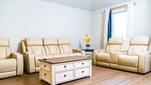 A room with two beige leather sofas, a wooden coffee table, and a small side table with a vase of yellow flowers. - Modern Family Retreat • 3BR/2BA • BBQ Patio • Designed for Comfort (Pea Ridge)