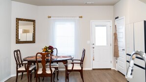 A dining area with a round table, four chairs, a mirror, and a window with blinds. - Modern Family Retreat • 3BR/2BA • BBQ Patio • Designed for Comfort (Pea Ridge)