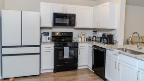 A modern kitchen with white cabinets, a black microwave, a stove, and a dishwasher. - Modern Family Retreat • 3BR/2BA • BBQ Patio • Designed for Comfort (Pea Ridge)