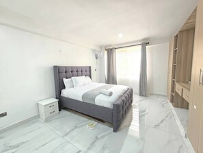 A bedroom with a bed, a nightstand, a wardrobe, and a window with curtains. - Serene 2-bedroom Apartment in Central Kisumu (Kisumu)