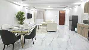 A modern living space with a dining area, a sofa, a TV, and a kitchen area. - Serene 2-bedroom Apartment in Central Kisumu (Kisumu)