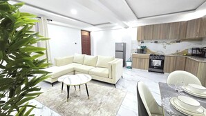 A modern living room with a sectional sofa, a round coffee table, and a dining area with a marble table and chairs. - Serene 2-bedroom Apartment in Central Kisumu (Kisumu)