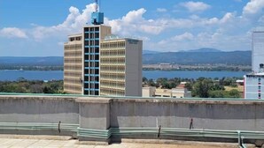 A rooftop terrace with a view of a cityscape, including a tall building with a blue top and a body with multiple windows. - Serene 2-bedroom Apartment in Central Kisumu (Kisumu)
