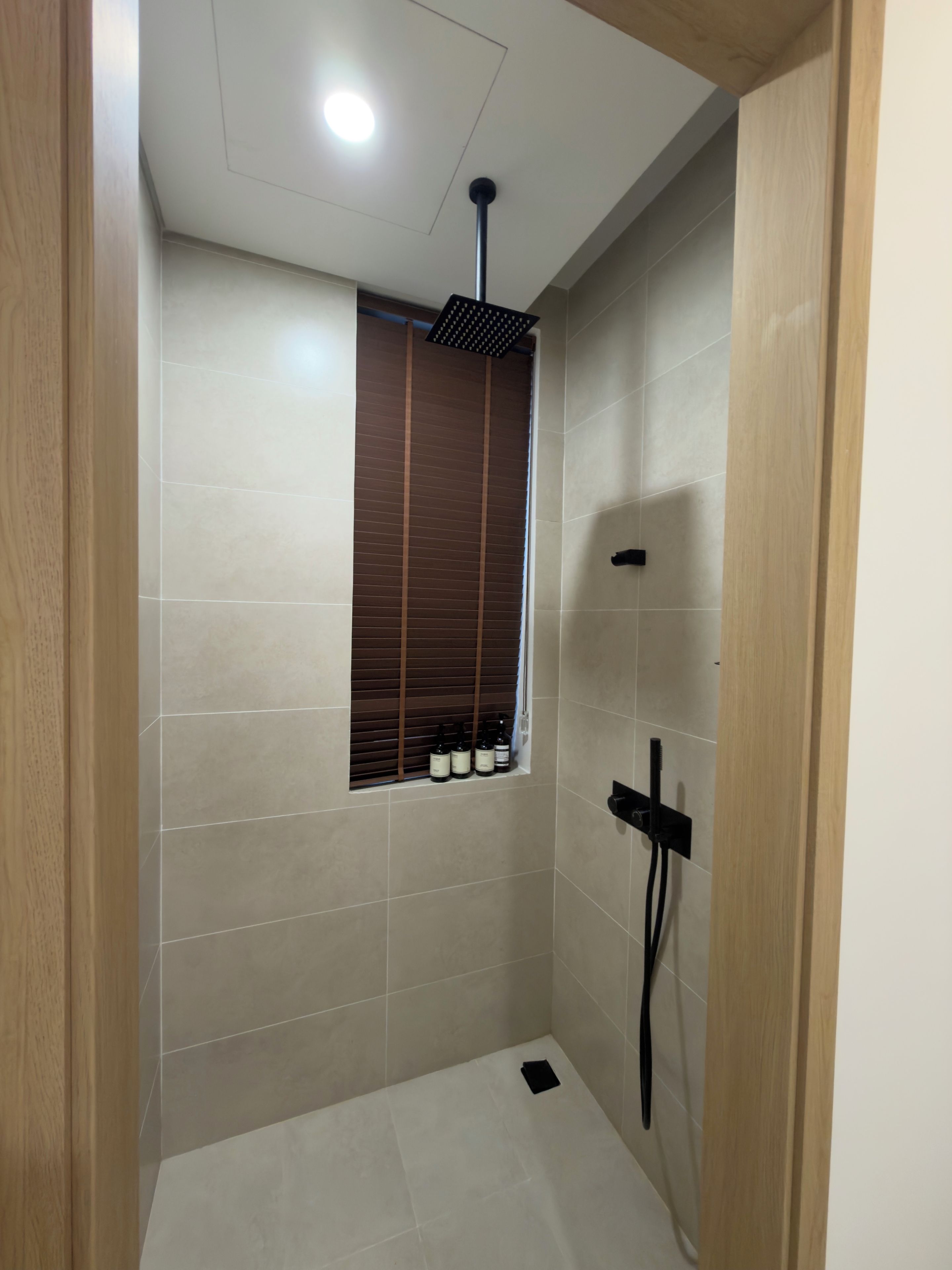 A shower with a window, tiled walls, and a ceiling light.